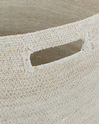Close-up of the Hawkins New York Essential Woven Hamper, made from handwoven seagrass with a rectangular cut-out handle. Its natural fibers and textured finish lend this laundry hamper a rustic, handcrafted appeal.