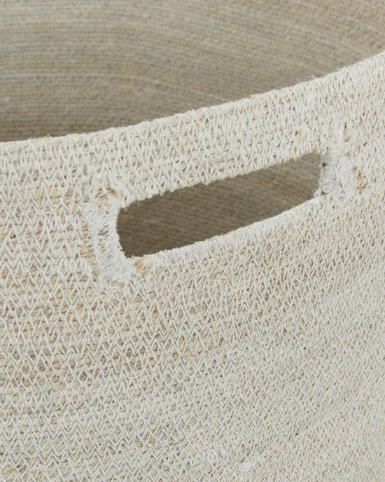 Close-up of the Hawkins New York Essential Woven Hamper, made from handwoven seagrass with a rectangular cut-out handle. Its natural fibers and textured finish lend this laundry hamper a rustic, handcrafted appeal.