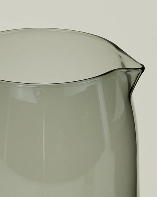 Close-up of the Hawkins New York Essential Glassware - Pitcher in Smoke, a 52 oz transparent grey-tinted pitcher with a subtle spout, set against a plain light background.