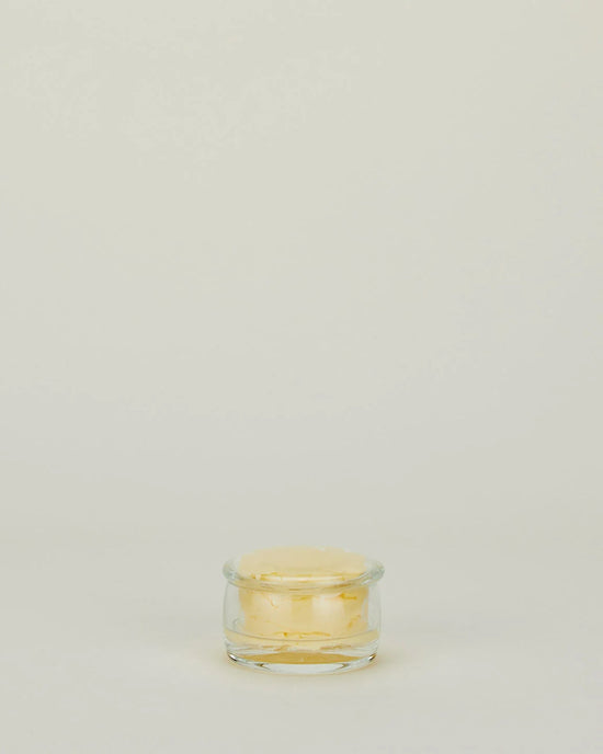 A Simple Glass Butter Keeper from Hawkins New York, filled with pale yellow butter, sits on a plain, light-colored background with ample empty space above.