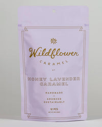 A lavender bag labeled Wildflower Caramel Co Honey Lavender Caramels contains 12 pieces of organic, handmade caramel with Texas honey. Gold, centered text highlights its sustainable sourcing.