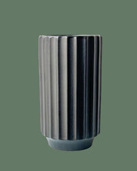 The Monroe Vase in Black by Jungle Club features vertical ridges and is displayed against a plain green background.