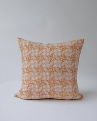 The Khushi Linen Pillow by Soil to Studio (18 x 18 in, Pastel Pink) features an intricate white and gold floral pattern inspired by Udaipur decor, set against a plain light grey background.