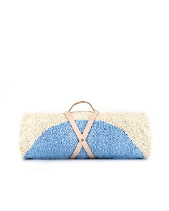 The Luna Lago - Blanket Roll by caminito is a rolled-up blue and off-white outdoor blanket with a light tan handmade leather strap and handle, shown against a plain white background.