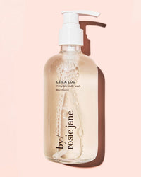A clear pump bottle of Leila Lou Everyday Body Wash by Rosie Jane sits against a light pink background, showcasing its hydrating clear liquid cleanser with visible bubbles inside.