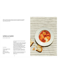 A bowl of eggs in tomato sauce with rustic bread rests on a striped cloth. On the left is a Uova al Sugo recipe from "La Nostra Cucina Povera – Everyday Italian Eats" by Cozy Publishing, featuring ingredients and instructions in English.