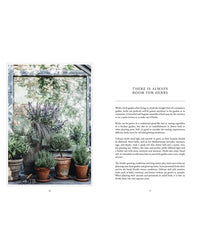 Living with Herbs" by Cozy Publishing inspires lush, organized herb gardening year-round, with potted plants arranged on wooden shelves and the floor in a sunlit greenhouse—perfect for enjoying homegrown herbs.