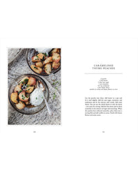 A bowl of caramelised peach slices with herbs and cream sits on a cloth next to another bowl, alongside the Living with Herbs recipe book by Cozy Publishing, featuring a recipe for caramelised thyme peaches.