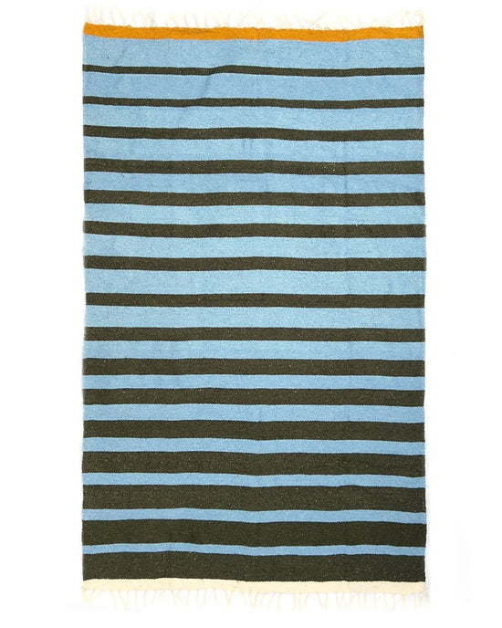 The caminito Marea Lago - Blanket Roll is a rectangular handwoven blanket from Mexico with alternating light blue and dark green stripes, a yellow accent stripe, and white fringe along both the top and bottom edges. Suitable for indoor or outdoor use.