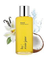 A bottle of Rosie Jane Madie Everyday Hydrating Body Oil sits before a white orchid, vanilla pods, half a coconut, and a splash of water, showcasing its natural ingredients and hydrating benefits.