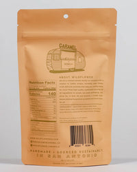 Tan resealable bag featuring a sketched camper and "Maple Whiskey Caramels" at the top. Wildflower Caramel Co—a Texas-based, women-owned company—features nutrition facts and sourcing info on the back.