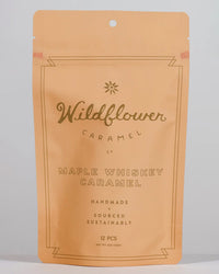 A tan resealable pouch from Wildflower Caramel Co labeled Maple Whiskey Caramels in A Bag contains 12 handmade, Texas-made, and sustainably sourced whiskey caramels.