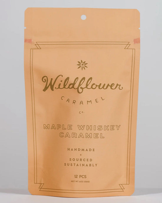 A tan resealable pouch from Wildflower Caramel Co labeled Maple Whiskey Caramels in A Bag contains 12 handmade, Texas-made, and sustainably sourced whiskey caramels.
