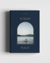Nordic Magic by Cozy Publishing is a dark blue book featuring an arched window on the cover with a person standing in a calm lake, distant hills, and a clear sky—evoking nature worship and Nordic traditions.
