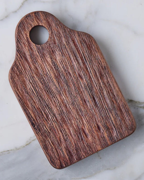 The etúHOME Dutch Small Cheese Board w/ Spreader in Natural, featuring a handle and round hole, is displayed on a light marble surface—an ideal and stylish hostess gift.