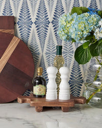 The etúHOME Normandy Wood Riser Footed Tray, Small, showcases a vinegar bottle, wine bottle, salt and pepper shakers, and a glass vase with blue hydrangeas on a marble counter set against blue leaf-patterned wallpaper.