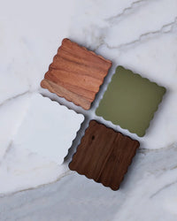 The etúHOME Scalloped Wood Coasters S/4 in Vineyard Colors are artfully arranged on a white marble surface, showcasing responsibly sourced wood in elegant white and olive tones.