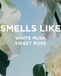 Close-up of dewy white roses against a blue sky, with “SMELLS LIKE WHITE MUSK SWEET ROSE” in bold white letters and a subtle mention of Rosie Everyday Body Milk by Rosie Jane, highlighting hydration in every petal.