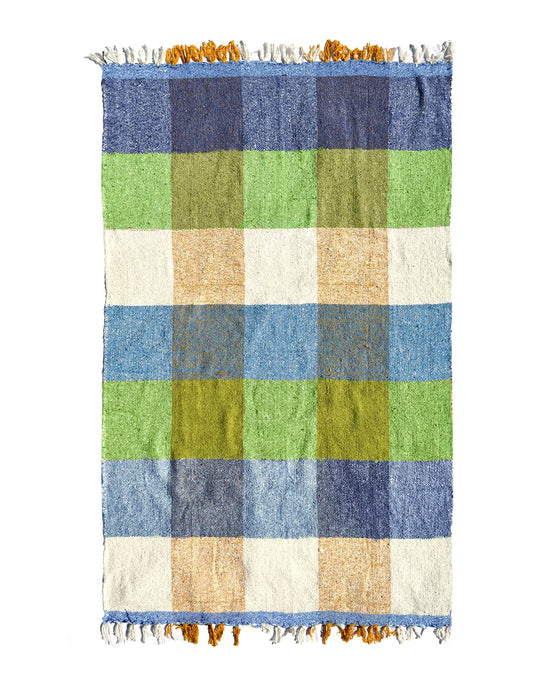 The Suave Kiwi - Blanket Roll by caminito is an ultra-soft, handwoven Mexican throw with a large blue, green, yellow, and white checkered pattern plus white/yellow fringe—perfect for indoor or outdoor use.