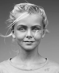 Black and white portrait of a young person with light hair blowing in the wind, embodying surf culture, wearing a simple shirt against a plain background. From "Surf Tribe" by Simon & Schuster.