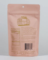 A pink, resealable pouch with gold accents displays Wildflower Caramel Co's Salted Caramels in A Bag, featuring product details, nutrition facts, ingredients, barcode, and notes on its handmade, sustainably sourced San Antonio origins.