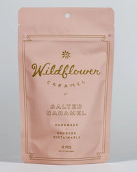 A pink resealable pouch from Wildflower Caramel Co labeled "Salted Caramels in A Bag" contains 12 handmade, sustainably sourced Texas caramels. The simple design features gold text and a small flower graphic.