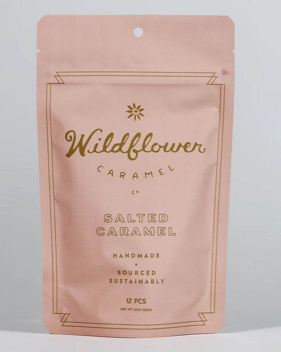 A pink resealable pouch from Wildflower Caramel Co labeled "Salted Caramels in A Bag" contains 12 handmade, sustainably sourced Texas caramels. The simple design features gold text and a small flower graphic.