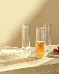 Four Pebbled Stemless Flutes by The Collective are arranged on a light surface, one filled with amber liquid, with a few red grapes resting on a nearby napkin. This set of 4 combines style and function for any occasion.