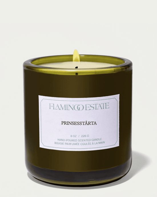 A green Flamingo Estate Prinsesstarta Candle featuring a single wick and a white label describes its almond marzipan scent. The candle is unlit and placed against a plain background.