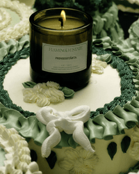 A green and white cake with icing flowers and a bow, topped with a lit Flamingo Estate Prinsesstarta Candle in a green glass jar.