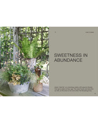On a wooden table outdoors, The Potted Garden - All Year Round by Cozy Publishing features a rustic metal bucket and pail with ferns and wildflowers; beside it, “Sweetness in Abundance” appears with a floral description below.