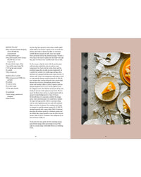 Two plates with slices of yellow vegan cheesecake from Vegalicious Cheesecakes – Bakery-Style & Plant-Based by Cozy Publishing are on a white tablecloth, surrounded by utensils, a fork, decorative leaves, and printed recipe instructions.
