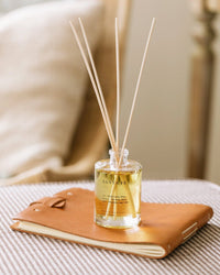 The Santa Fe Reed Diffuser by Brooklyn Candle Studio rests on a tan leather notebook atop checkered fabric, with a softly blurred background.