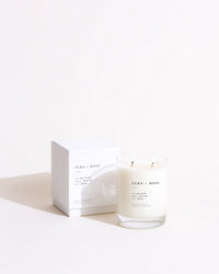 The Fern + Moss Classic 2-Wick Candle by Brooklyn Candle Studio rests next to its matching white box on a light surface, showcasing a simple, modern design with black text and minimalistic style.