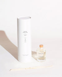 The Brooklyn Candle Studio Santa Fe Reed Diffuser features a luxury fragrance in a clear glass bottle with a wooden cap, reed sticks, and comes in a white cylindrical box—perfect for minimalist decor.