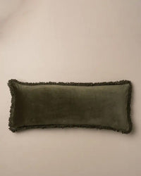 The Saarde Velvet Body Pillow w/ Feather Insert in Dark Olive features a long, rectangular shape with fringe trim, shown on a neutral beige background.