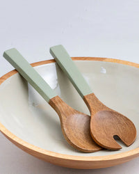 The Madras Serving Set in Sage by Be Home US features handcrafted mango wood servers with green handles, elegantly placed inside a beige ceramic bowl with a wooden rim—an heirloom-quality piece made from sustainable materials.
