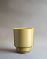 The Bergs Potter Hoff Glazed 5.5 inch Pot in Pale Yellow, featuring a glossy finish and Scandinavian-inspired design, sits on a neutral gray surface with a simple gray background.