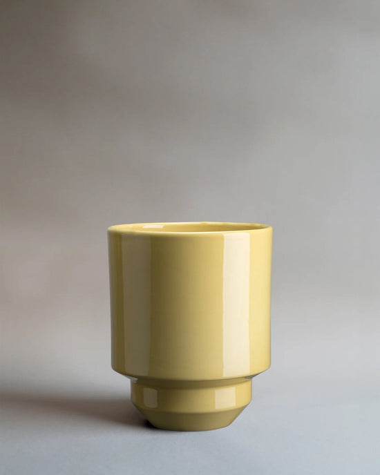 The Bergs Potter Hoff Glazed 5.5 inch Pot in Pale Yellow, featuring a glossy finish and Scandinavian-inspired design, sits on a neutral gray surface with a simple gray background.