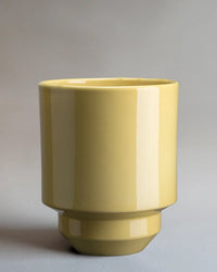 The Bergs Potter Hoff Glazed 7.1 inch Pot in Pale Yellow features a glossy, cylindrical ceramic design with a wide opening, narrow base, and Scandinavian-inspired style, set against a plain gray background.