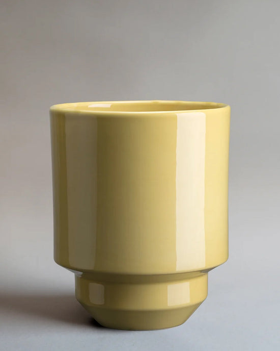 The Bergs Potter Hoff Glazed 7.1 inch Pot in Pale Yellow features a glossy, cylindrical ceramic design with a wide opening, narrow base, and Scandinavian-inspired style, set against a plain gray background.