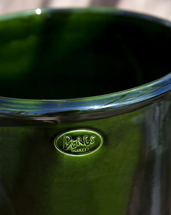 The Modena Glazed 13.8 inch Cachepot by Bergs Potter features a shiny Emerald Green finish with the Bergs Potter logo embossed near the rim—perfect as a stylish indoor planter for your home.