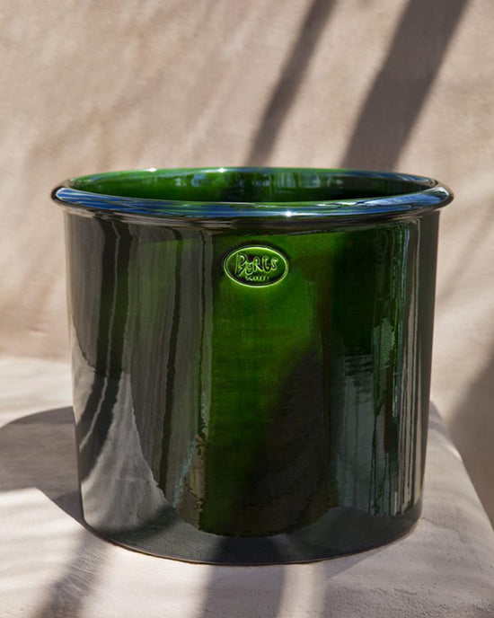 The Bergs Potter Modena Glazed 13.8 inch Cachepot in Emerald Green features a glossy finish and a small embossed front label, displayed on a neutral surface with subtle shadow patterns.