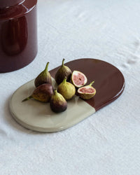 The Bergs Potter Nuna Glazed 13.4 x 7.9 Tray in Sandstone/Deep Burgundy holds whole and halved figs on a light fabric surface.