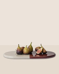 Six figs, one sliced, are displayed on the Nuna Glazed 13.4 x 7.9 Tray in Sandstone/Deep Burgundy by Bergs Potter. This elegant, food-safe stoneware piece pairs beautifully with Nuna Coasters against a neutral backdrop.