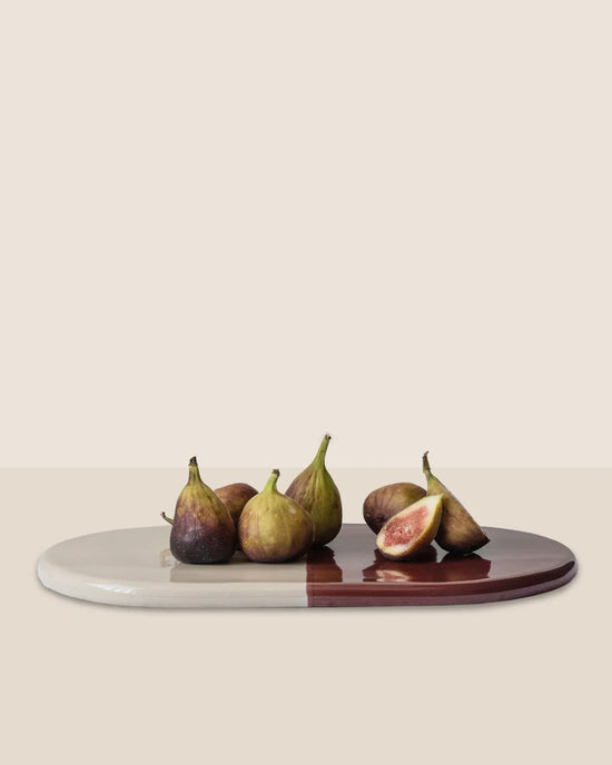 Six figs, one sliced, are displayed on the Nuna Glazed 13.4 x 7.9 Tray in Sandstone/Deep Burgundy by Bergs Potter. This elegant, food-safe stoneware piece pairs beautifully with Nuna Coasters against a neutral backdrop.