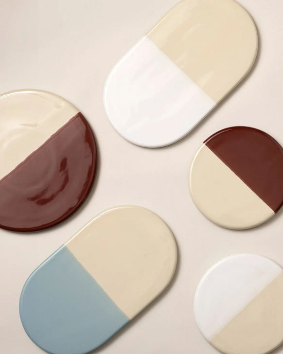 The Nuna Glazed 13.4 x 7.9 Tray in Sandstone/Mineral White by Bergs Potter is beautifully arranged on a light surface, creating a coordinated table setting when paired with complementary glazed stoneware coasters.