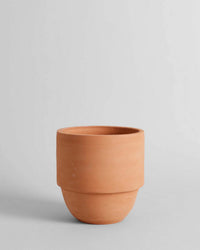 The Bloomist Big Cuff Planter | Large is a plain, unglazed terracotta planter set on a neutral surface against a light gray background—perfect for anyone seeking timeless, handmade design.