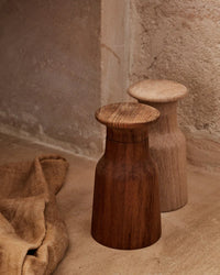 The Hammer Grinder | Teak by Bloomist, featuring one dark teak and one light wooden grinder, stands side by side on a textured stone surface next to a brown cloth, showcasing classic Danish design.