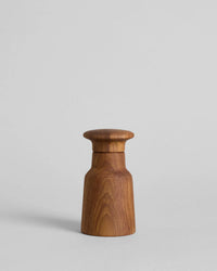 The Hammer Grinder | Teak by Bloomist is a small, smooth wooden salt and pepper grinder with a cylindrical base and rounded top, inspired by Danish design, shown on a plain light gray background.